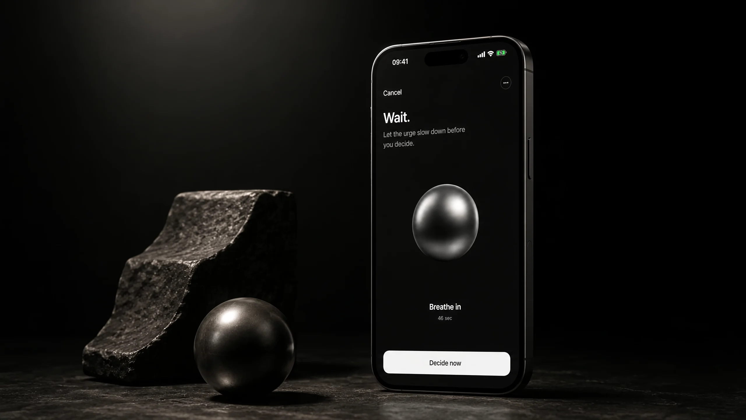 Axyom — a dark iPhone standing on stone showing the pause screen: Wait. Let the urge slow down before you decide. A metallic sphere rests beside it.
